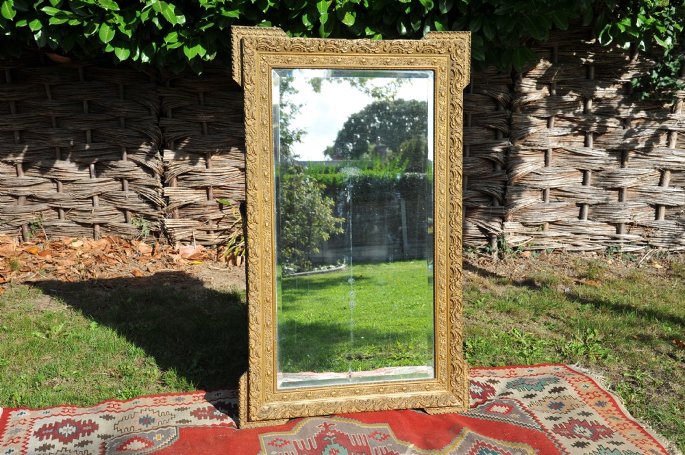 A large rectangular 19th-century French wall mirror featuring an ornate gold gilt gesso frame with floral relief details and bevelled glass. View II