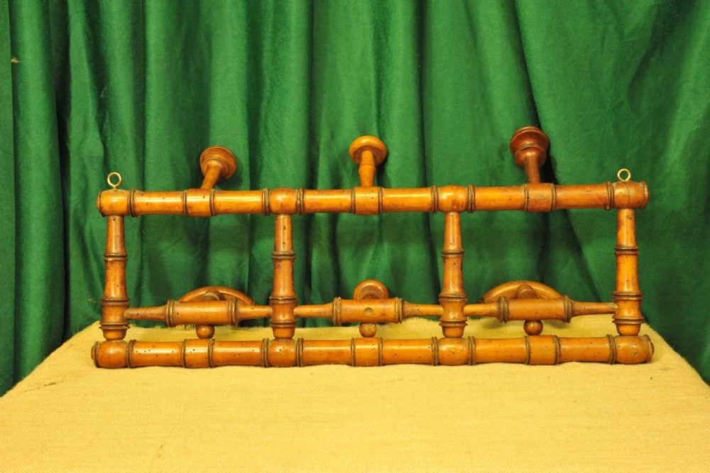 A golden brown turned wood wall-mounted coat rack with six pegs styled in a faux bamboo lattice frame with brass hanging rings.