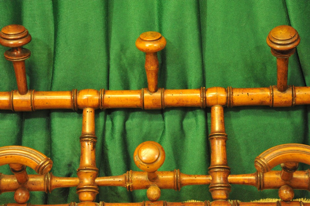 A golden brown turned wood wall-mounted coat rack with six pegs styled in a faux bamboo lattice frame with brass hanging rings. View II
