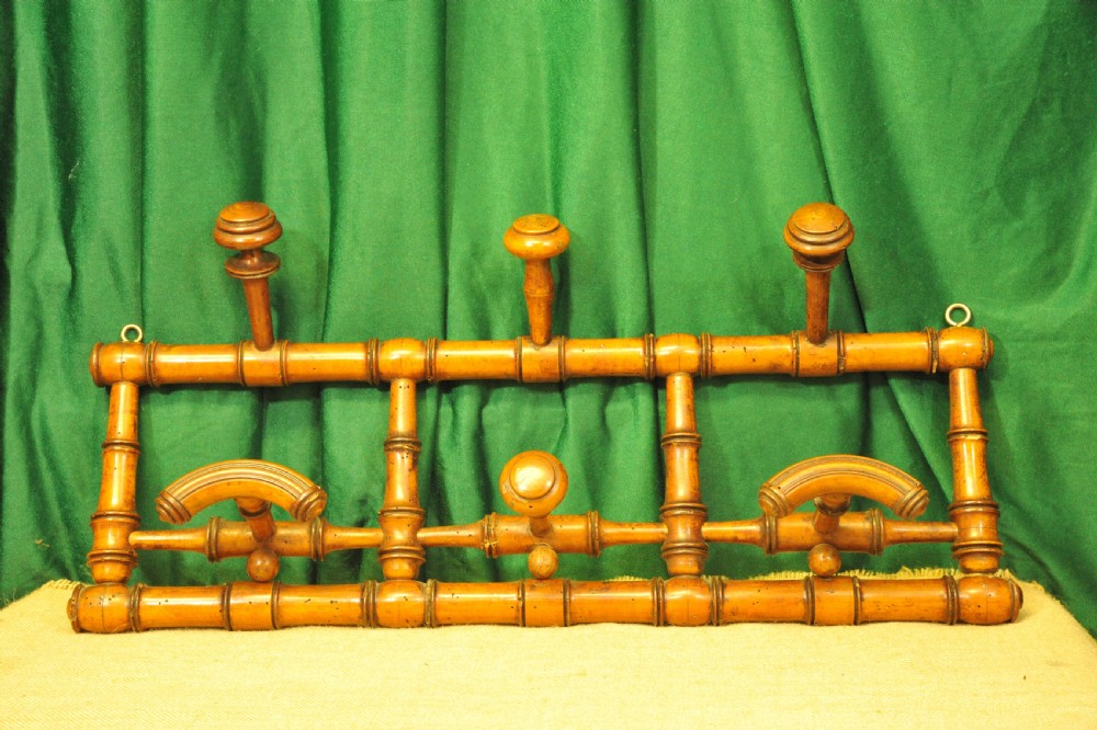A golden brown turned wood wall-mounted coat rack with six pegs styled in a faux bamboo lattice frame with brass hanging rings. View III