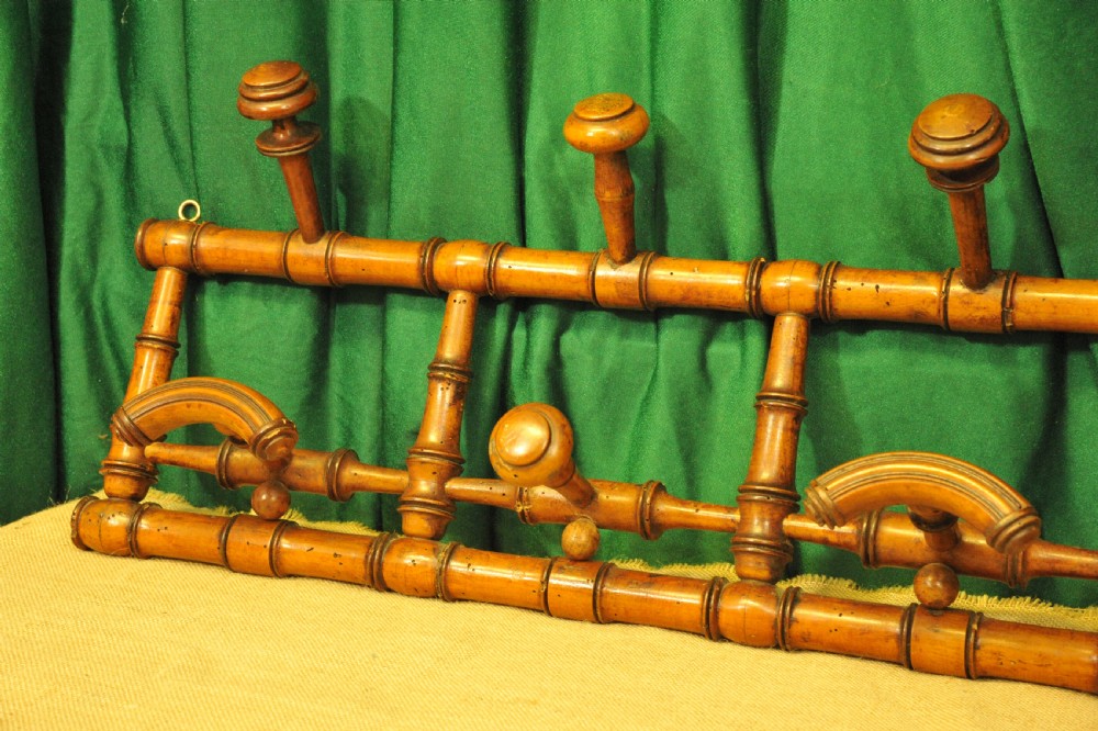 A golden brown turned wood wall-mounted coat rack with six pegs styled in a faux bamboo lattice frame with brass hanging rings. View V