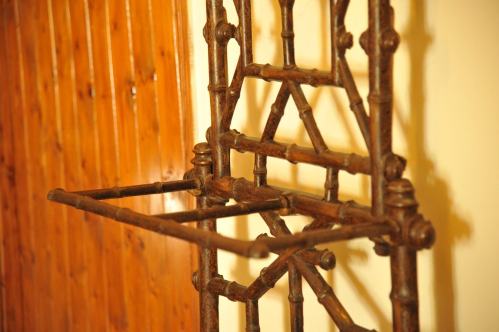 A late nineteenth-century French cast iron hall stand featuring a faux bamboo frame, central mirror, coat hooks, umbrella rail, and dual drip trays. View V