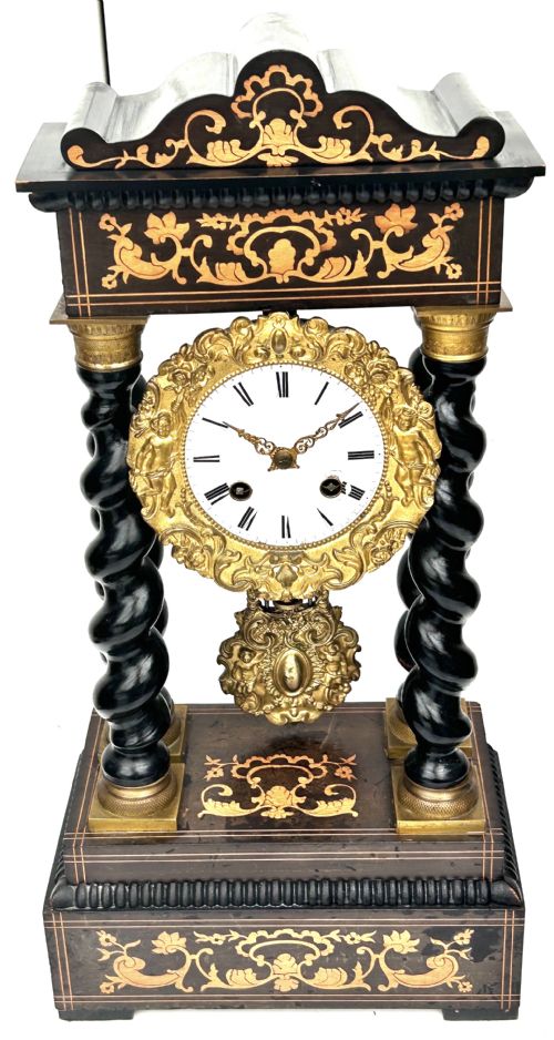 fig 1. An antique French Empire ebonised and marquetry portico clock featuring four barley twist columns, gilt bronze capitals, an ornate ormolu framed enamel dial, and a decorative pendulum.