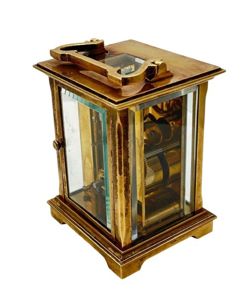 fig 2. A rectangular brass Matthew Norman carriage clock with bevelled glass sides, a top carrying handle, and a white enamel dial displaying Roman numerals.