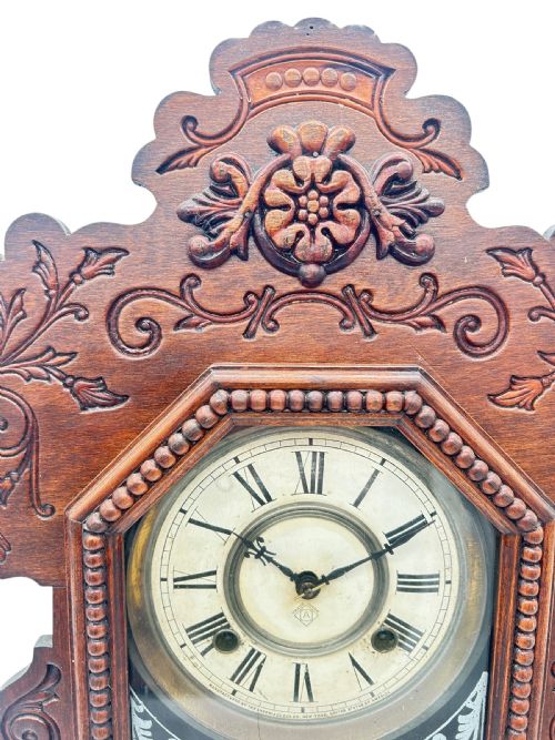 fig 1. A late 19th-century Ansonia gingerbread mantel clock crafted from dark carved oak with a stencilled glass pendulum door and Roman numeral dial.