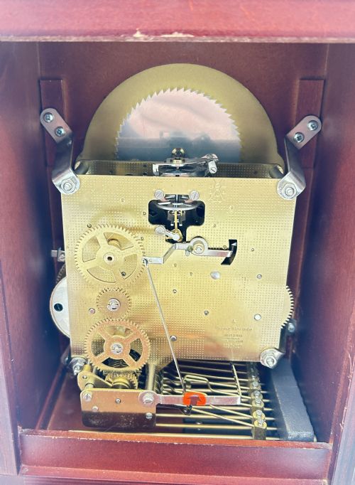 fig 1. A wooden bracket clock featuring a reddish mahogany case, brass carrying handle, and a decorative dial with moon phase indicator.