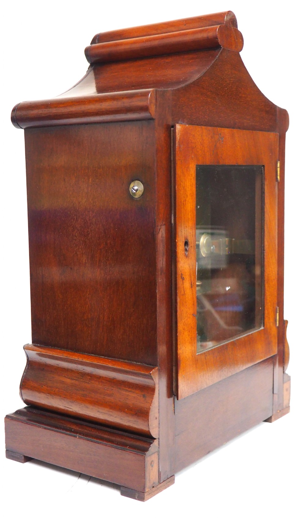 An antique Victorian flame mahogany bracket clock featuring carved leaf decoration, a round cream dial with Roman numerals, and a hinged brass bezel. View IX