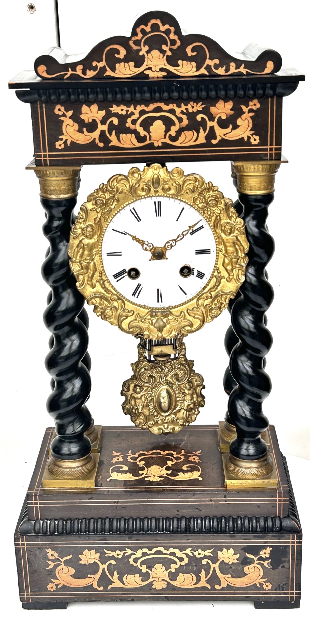 An antique French Empire ebonised and marquetry portico clock featuring four barley twist columns, gilt bronze capitals, an ornate ormolu framed enamel dial, and a decorative pendulum.
