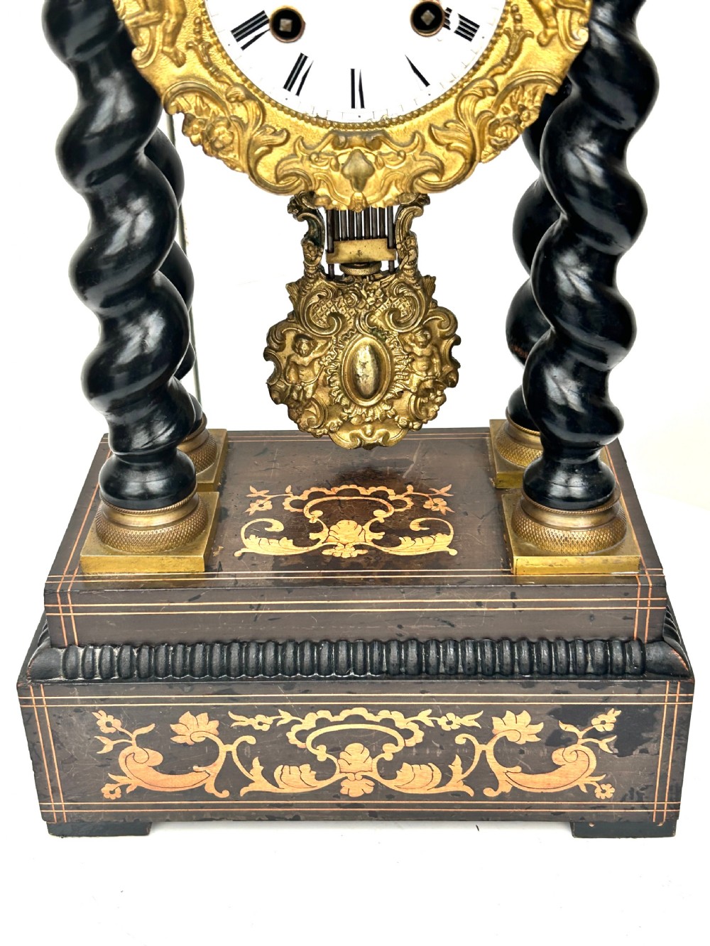An antique French Empire ebonised and marquetry portico clock featuring four barley twist columns, gilt bronze capitals, an ornate ormolu framed enamel dial, and a decorative pendulum. View V