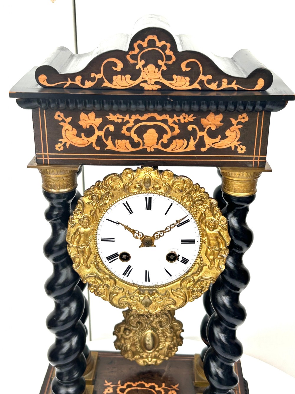 An antique French Empire ebonised and marquetry portico clock featuring four barley twist columns, gilt bronze capitals, an ornate ormolu framed enamel dial, and a decorative pendulum. View VII