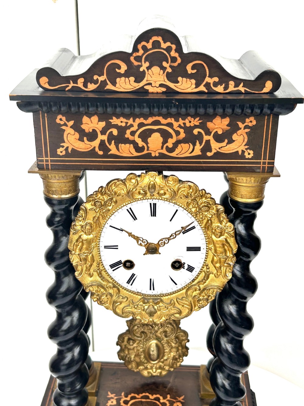 An antique French Empire ebonised and marquetry portico clock featuring four barley twist columns, gilt bronze capitals, an ornate ormolu framed enamel dial, and a decorative pendulum. View VIII