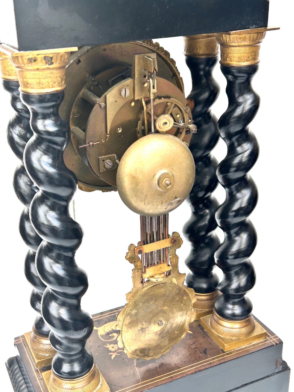 An antique French Empire ebonised and marquetry portico clock featuring four barley twist columns, gilt bronze capitals, an ornate ormolu framed enamel dial, and a decorative pendulum. View XII