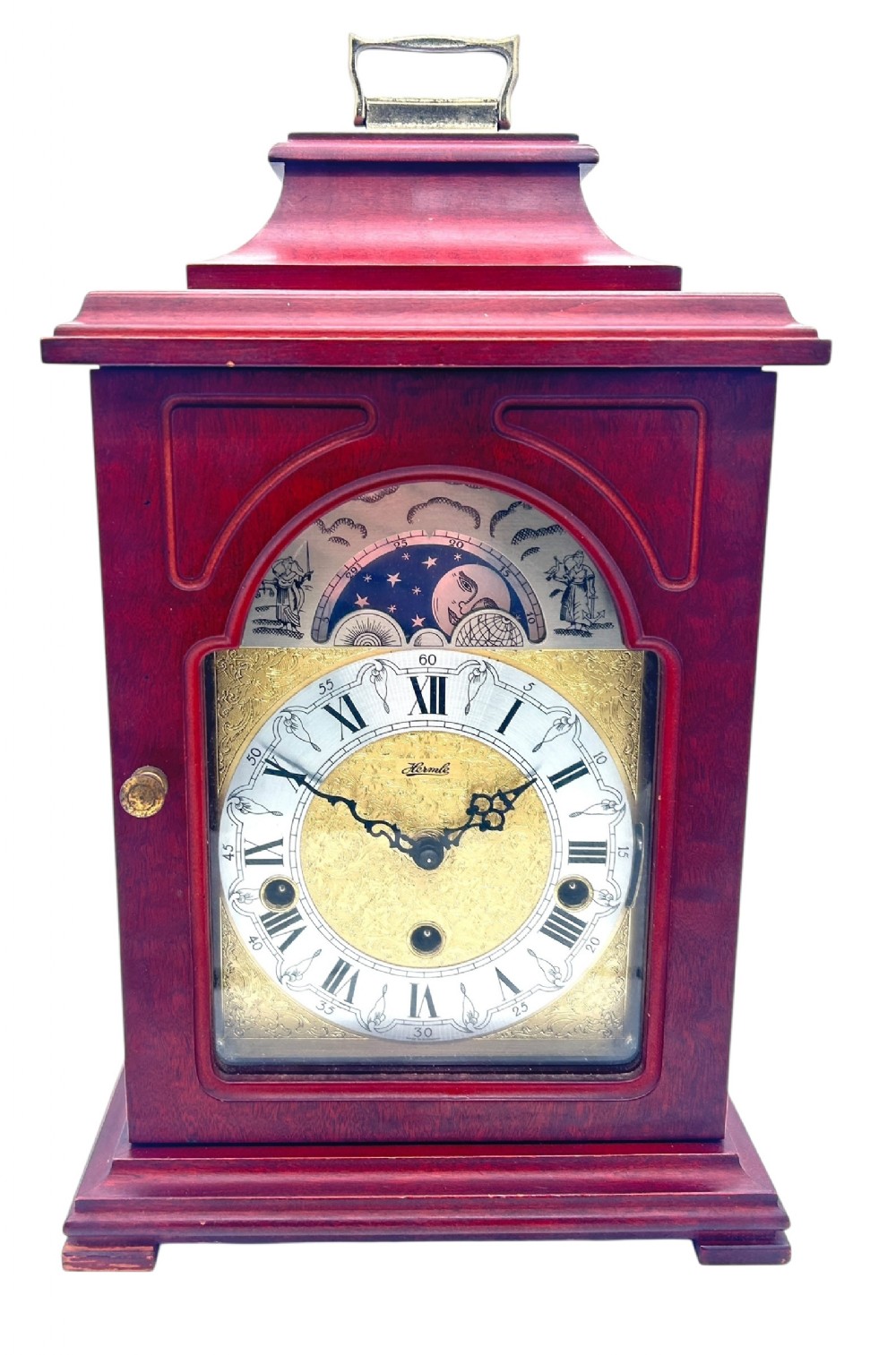 A wooden bracket clock featuring a reddish mahogany case, brass carrying handle, and a decorative dial with moon phase indicator.
