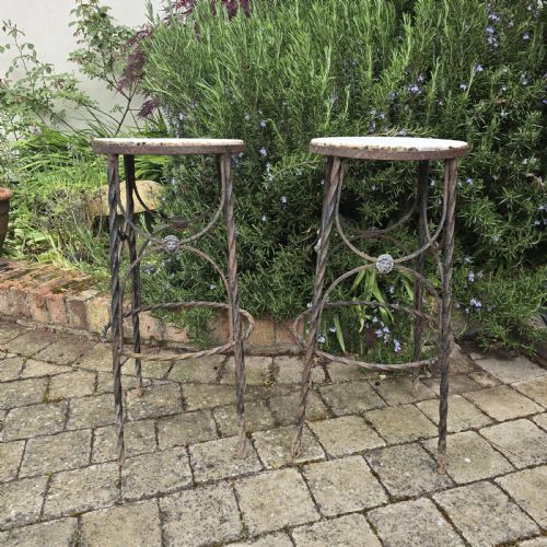 fig 1. A pair of tall wrought iron plant stands with circular stone tops, twisted legs, and central lion mask medallion details.