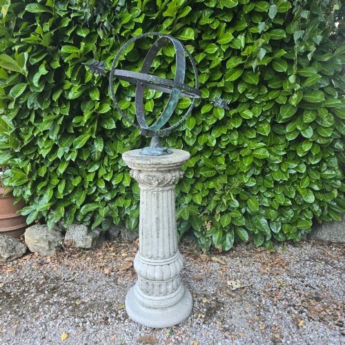 fig 1. A weathered metal armillary sphere with an arrow gnomon and verdigris patina mounted atop a carved fluted stone pedestal.
