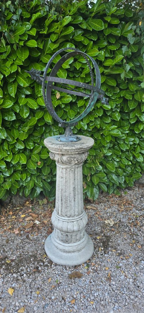 fig 2. A weathered metal armillary sphere with an arrow gnomon and verdigris patina mounted atop a carved fluted stone pedestal.
