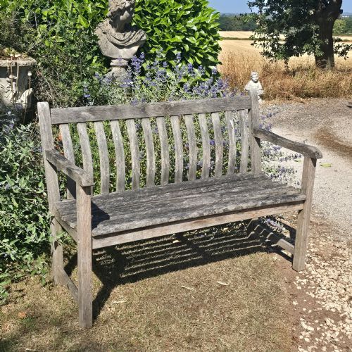 fig 1. A weathered teak garden bench featuring a vertical slatted backrest, slatted seat, and straight legs connected by stretchers.