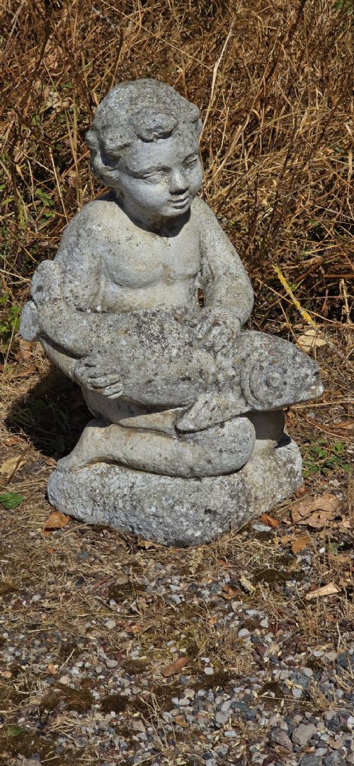 A weathered cast stone garden statue depicting a seated cherub holding a fish. View III