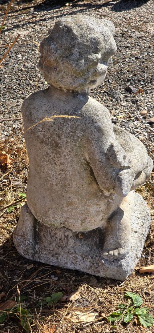 A weathered cast stone garden statue depicting a seated cherub holding a fish. View VI