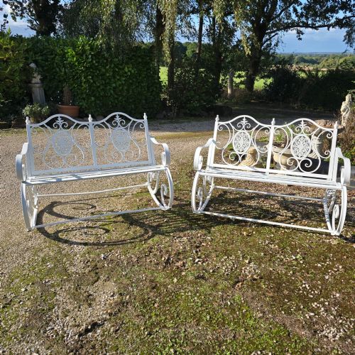 fig 1. A pair of restored white-painted wrought iron garden rocking benches featuring ornate decorative scrollwork backrests and slatted seats.