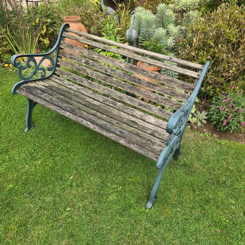 fig 1. A slatted wooden garden bench with dark green cast iron scrollwork end frames sitting on grass.