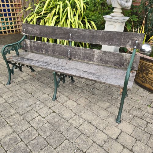 fig 1. A cast iron garden bench with dark green painted end supports and weathered grey timber slats forming the seat and backrest.