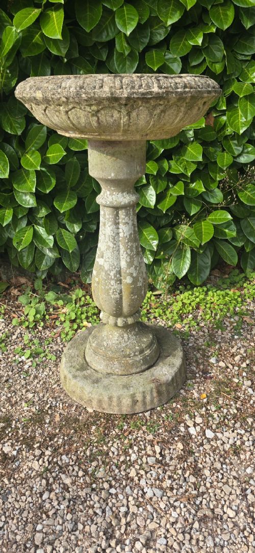 fig 1. A weathered grey stone bird bath featuring a shallow circular bowl with carved rim detail on a baluster pedestal and round stepped base.