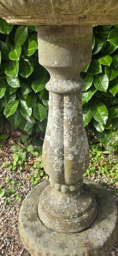 A weathered grey stone bird bath featuring a shallow circular bowl with carved rim detail on a baluster pedestal and round stepped base. View IV