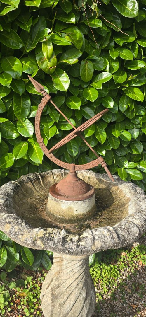 fig 1. A weathered stone bird bath featuring a spiral-carved pedestal support topped with a rust-brown cast iron armillary sphere.