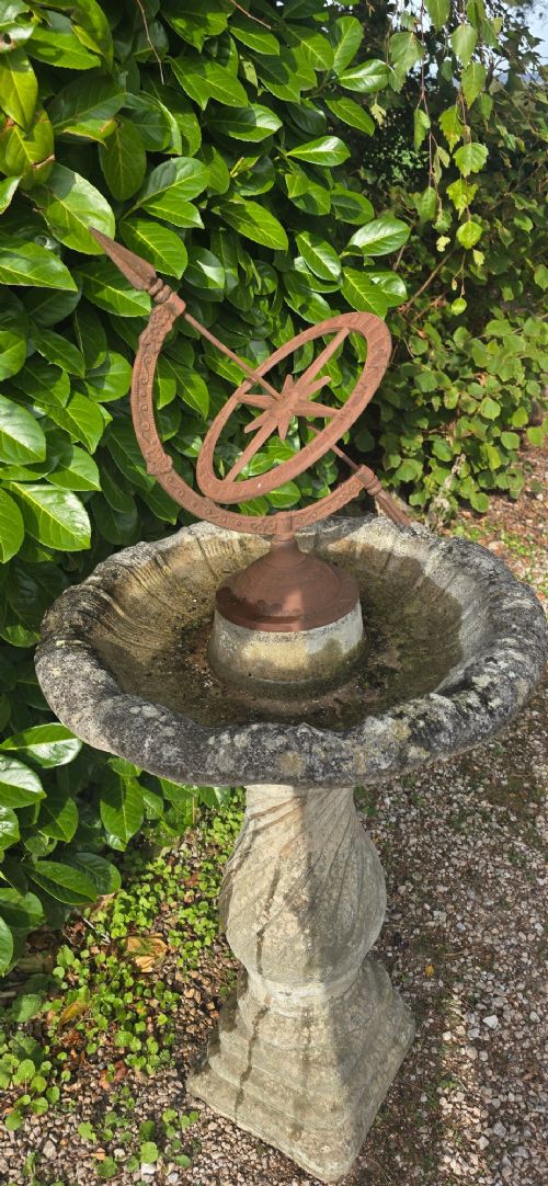 A weathered stone bird bath featuring a spiral-carved pedestal support topped with a rust-brown cast iron armillary sphere. View V