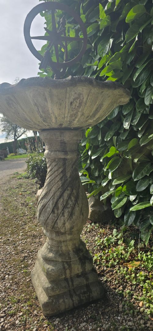 A weathered stone bird bath featuring a spiral-carved pedestal support topped with a rust-brown cast iron armillary sphere. View VII