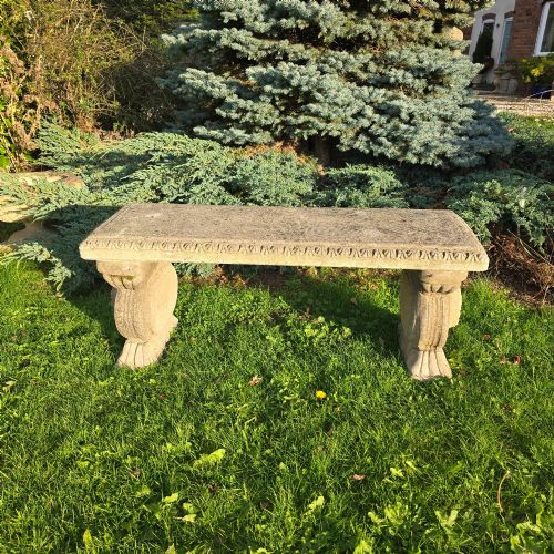 fig 1. A rectangular weathered stone garden bench featuring carved scroll supports set on lawn grass.