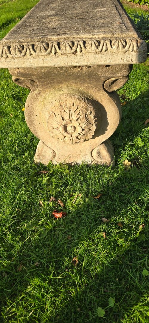 A rectangular weathered stone garden bench featuring carved scroll supports set on lawn grass. View VI
