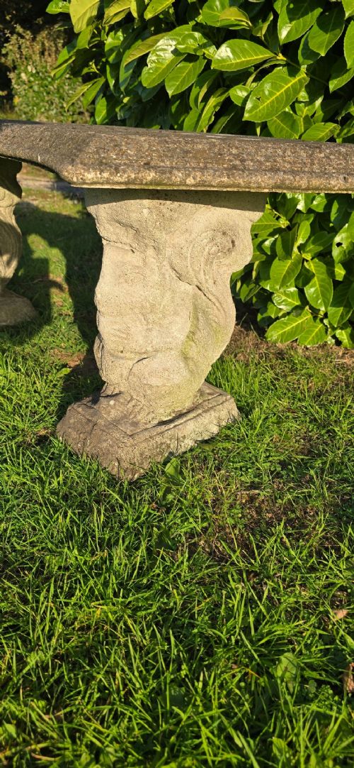 A curved weathered grey stone garden bench featuring a bevelled seat resting on two sculpted animal-form pedestal supports. View VI