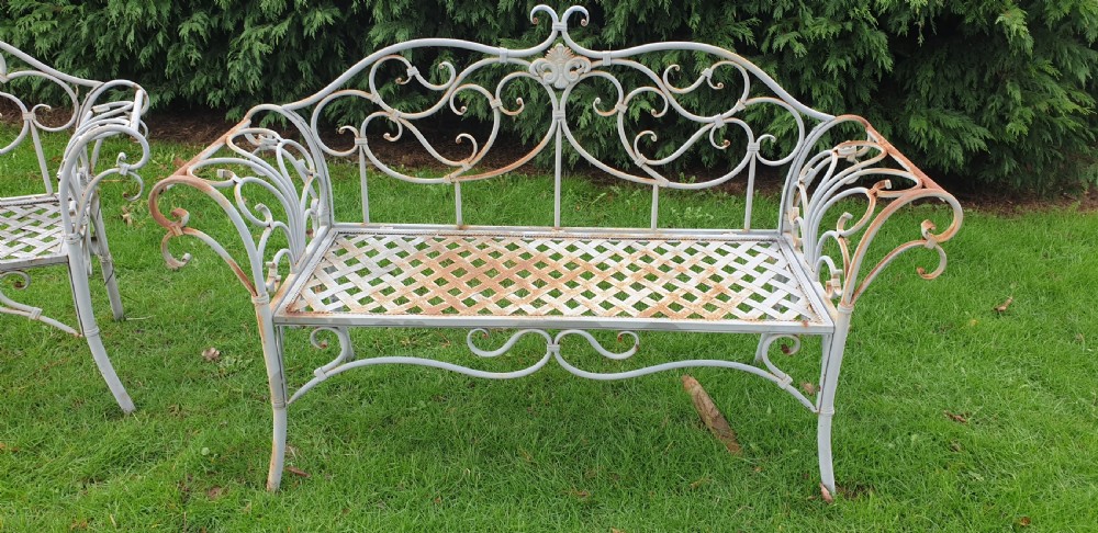 A pair of grey painted wrought iron garden benches featuring ornate scrollwork backrests and woven lattice seats. View II