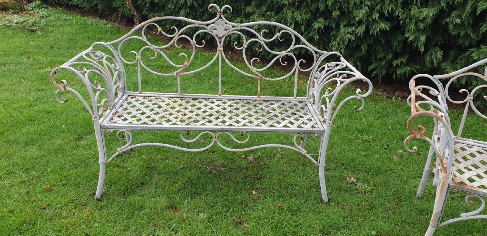 A pair of grey painted wrought iron garden benches featuring ornate scrollwork backrests and woven lattice seats. View V