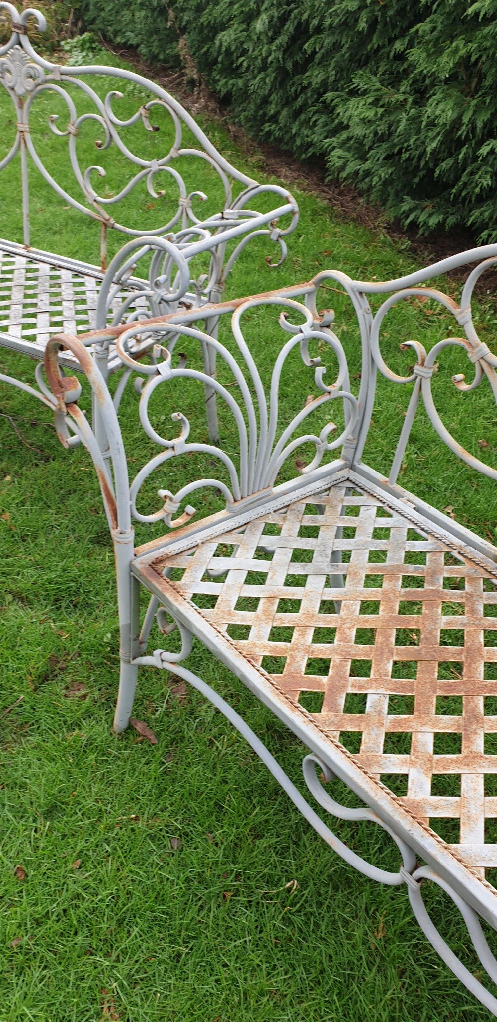 A pair of grey painted wrought iron garden benches featuring ornate scrollwork backrests and woven lattice seats. View VI