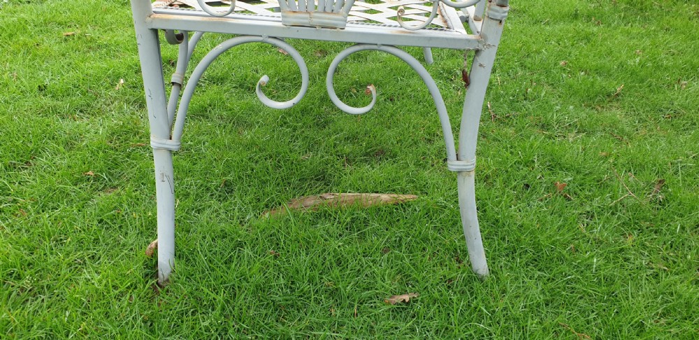 A pair of grey painted wrought iron garden benches featuring ornate scrollwork backrests and woven lattice seats. View VII