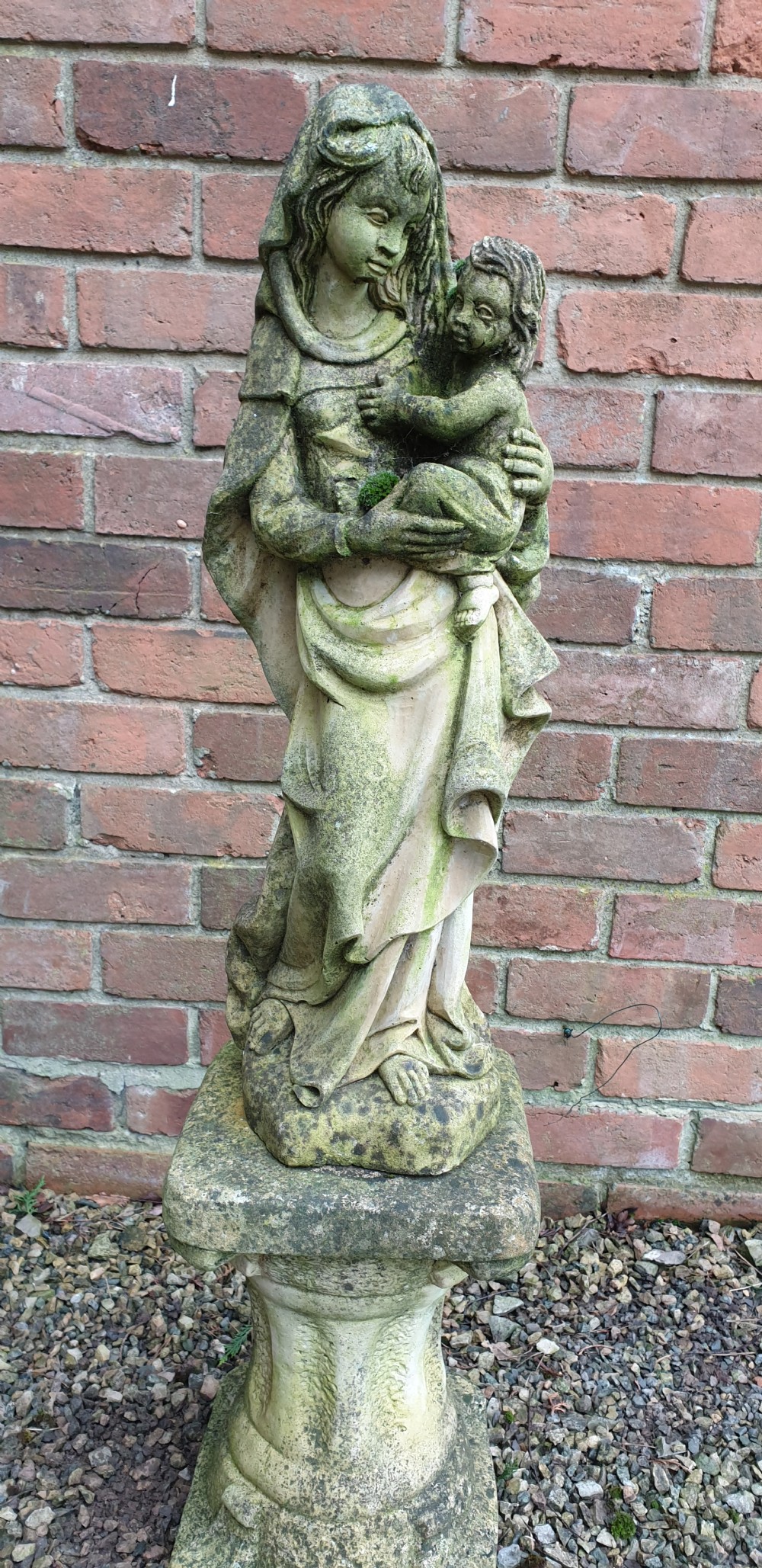 A pair of weathered grey stone statues depicting the Madonna and Child, each mounted on a square tapered plinth base. View V
