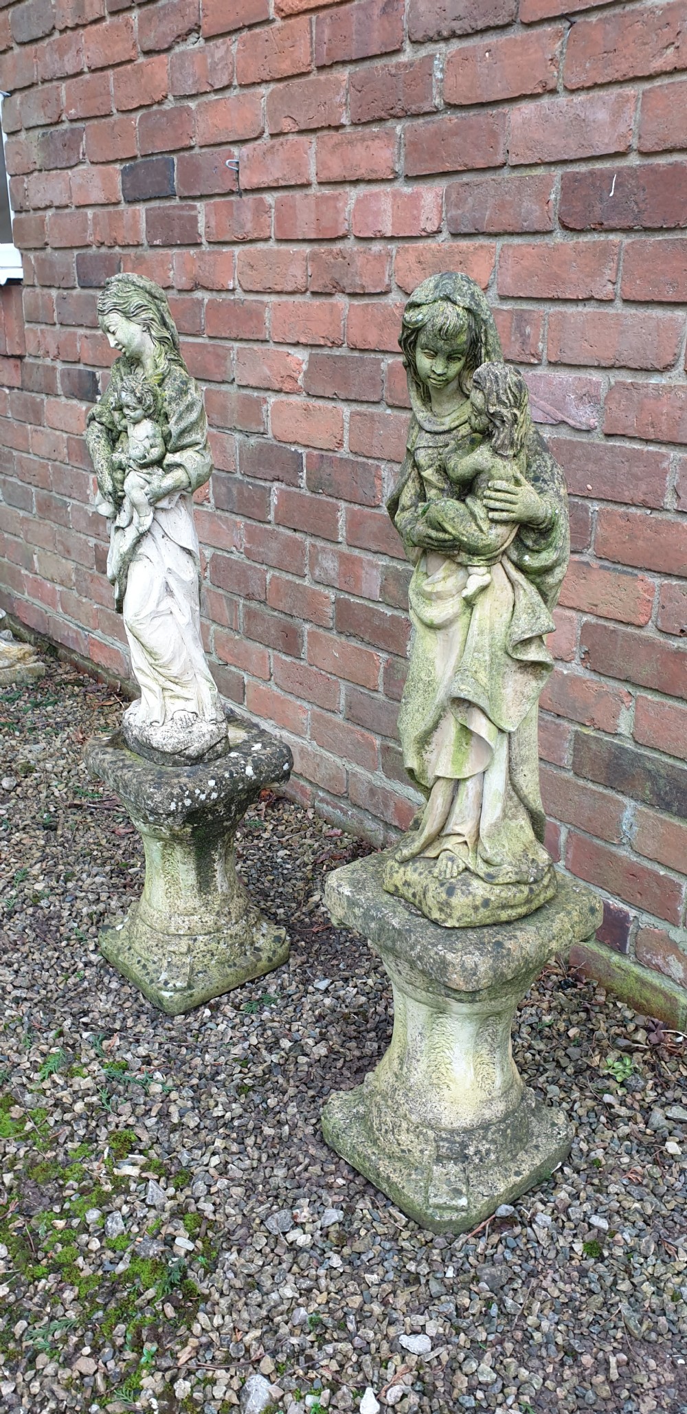 A pair of weathered grey stone statues depicting the Madonna and Child, each mounted on a square tapered plinth base. View VI