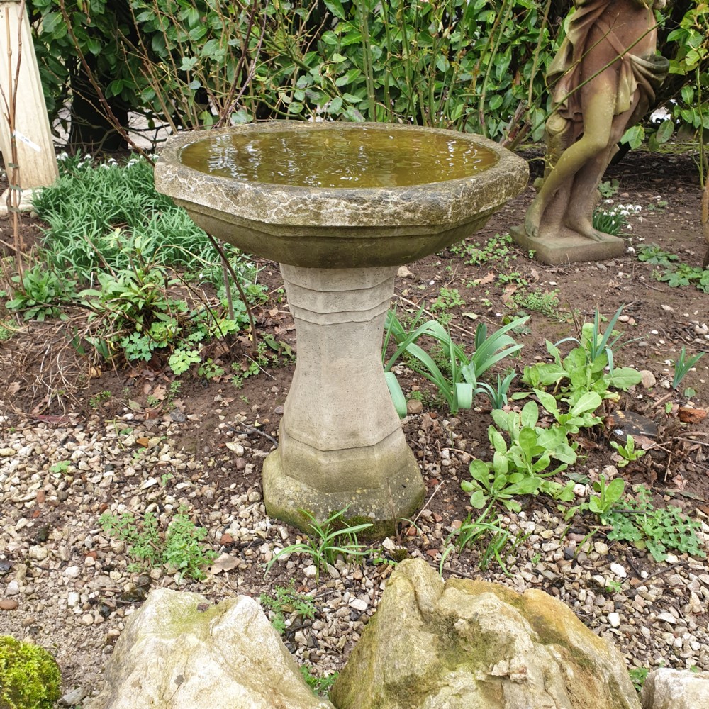 A weathered grey cast stone bird bath featuring an octagonal basin resting upon a tapered faceted pedestal base.