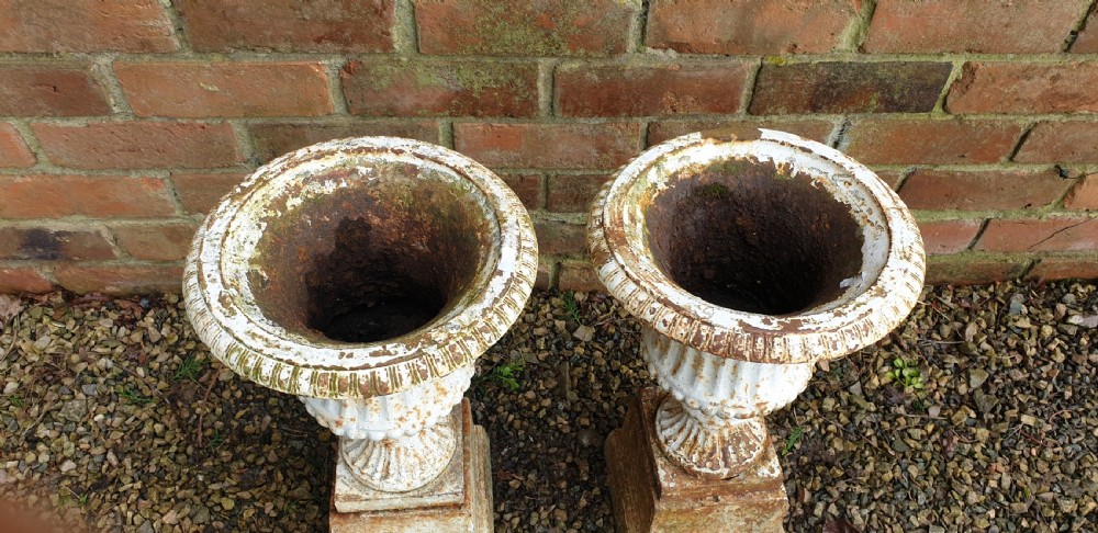 A pair of weathered white-painted cast iron urns with fluted bodies resting on square plinth bases. View II
