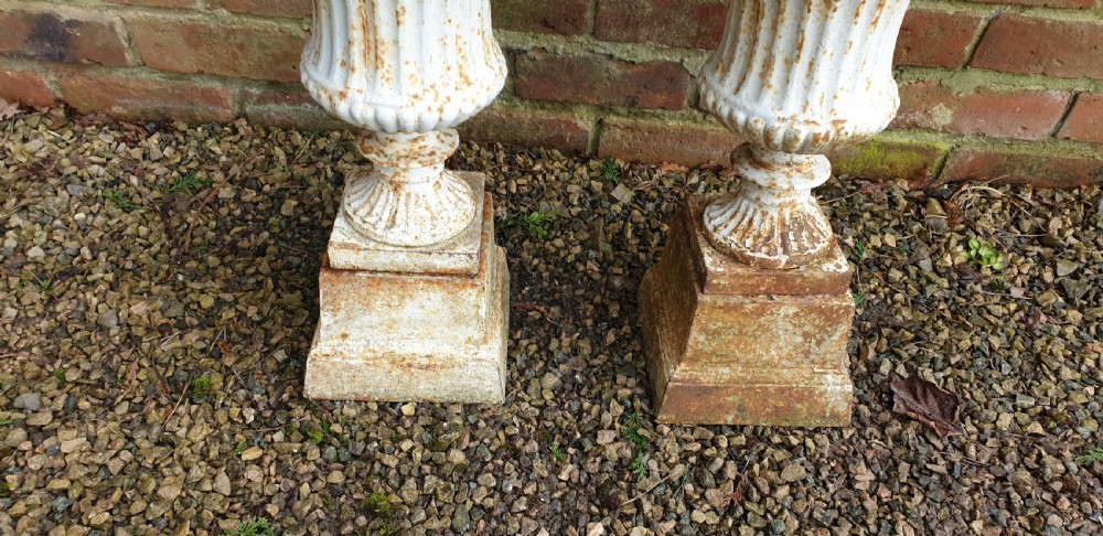 A pair of weathered white-painted cast iron urns with fluted bodies resting on square plinth bases. View III