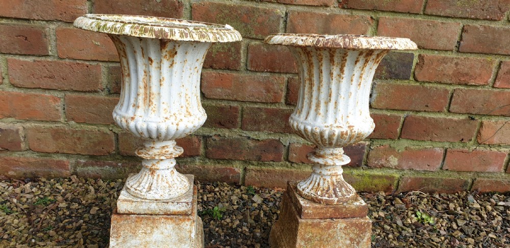 A pair of weathered white-painted cast iron urns with fluted bodies resting on square plinth bases. View IV