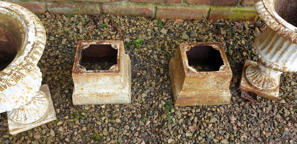 A pair of weathered white-painted cast iron urns with fluted bodies resting on square plinth bases. View V