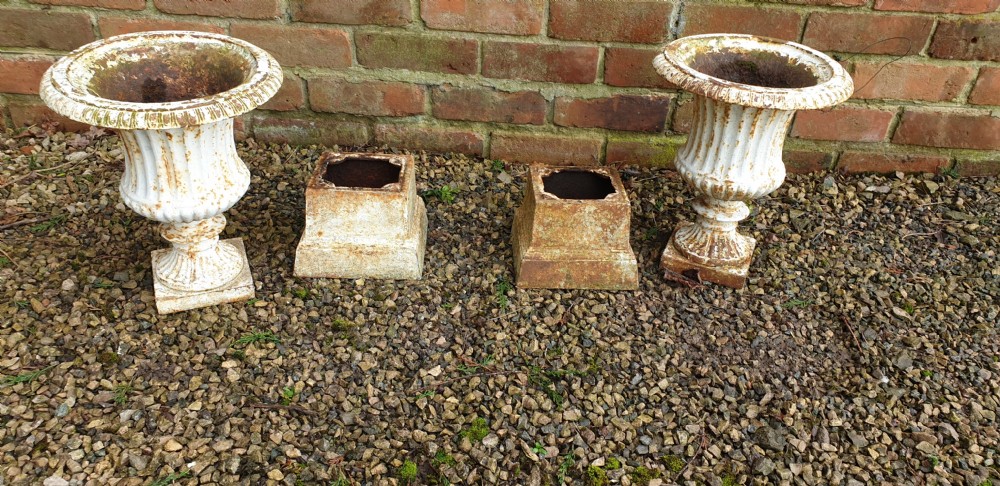 A pair of weathered white-painted cast iron urns with fluted bodies resting on square plinth bases. View VI