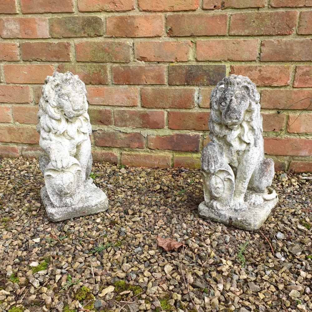 A pair of weathered grey stone finials sculpted as seated lions holding shields on integral rectangular bases.