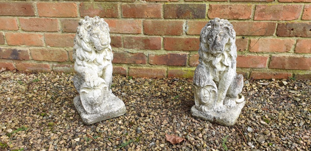 A pair of weathered grey stone finials sculpted as seated lions holding shields on integral rectangular bases. View II