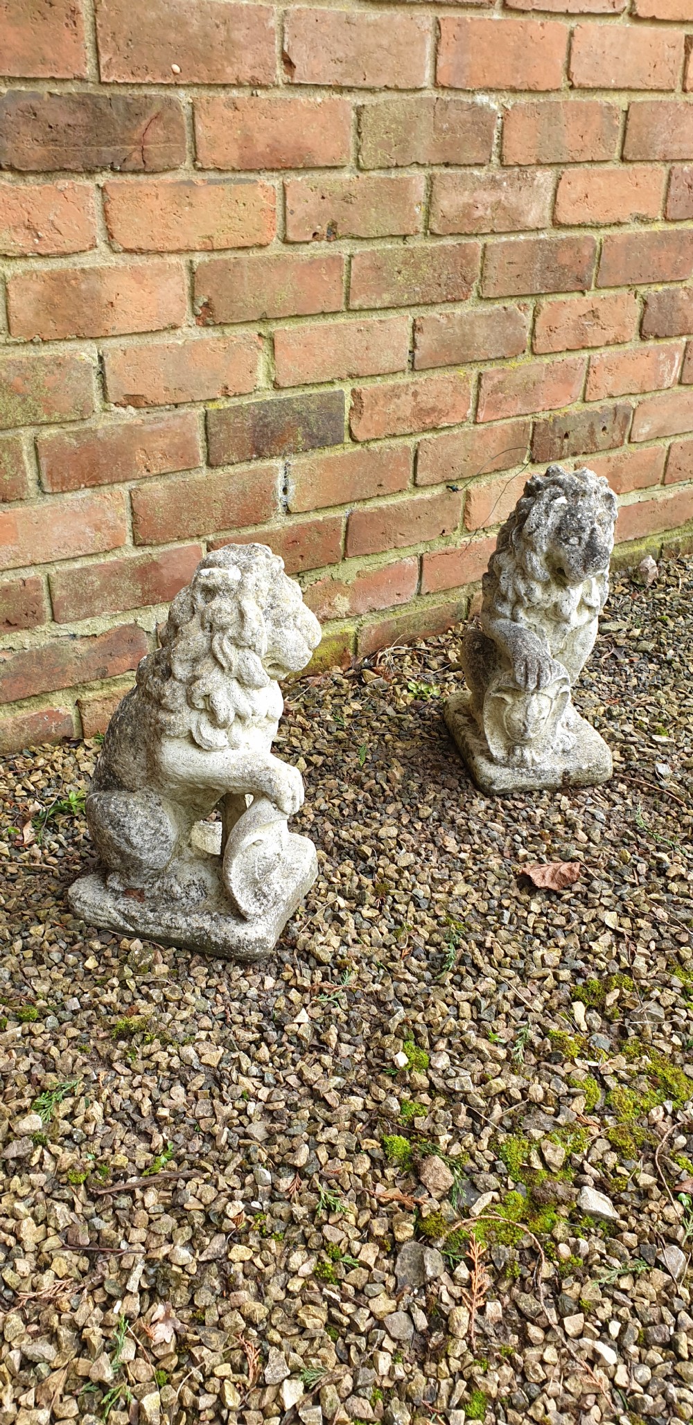 A pair of weathered grey stone finials sculpted as seated lions holding shields on integral rectangular bases. View III