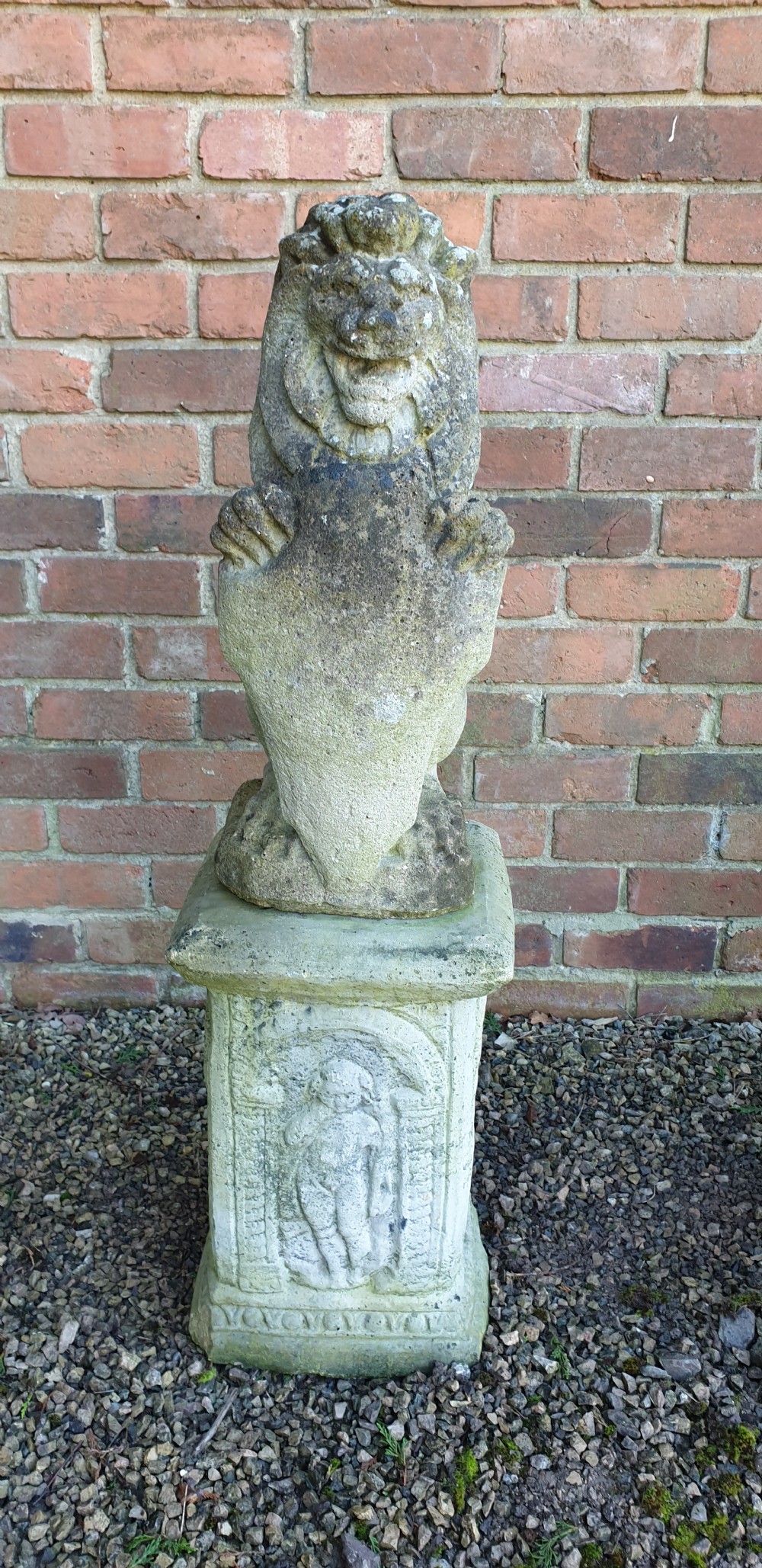 A pair of weathered grey stone seated lion statues holding shields, mounted on relief-carved rectangular plinths. View II